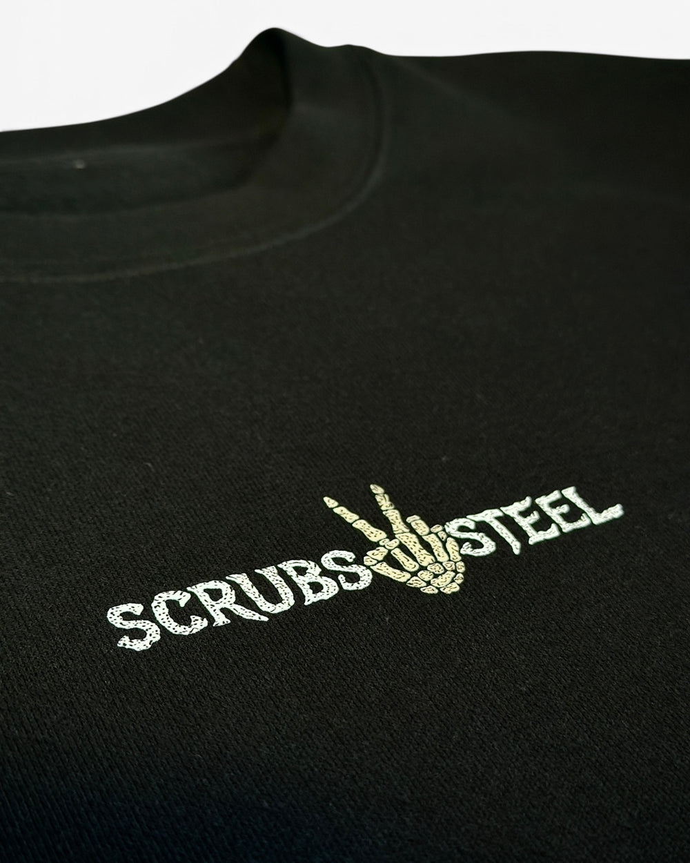 Detail of the Scrubs and Steel chest wordmark with the skeleton hand throwing a peace sign