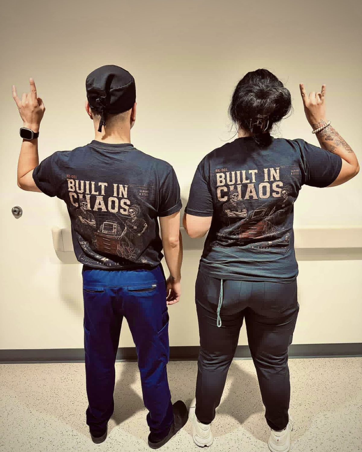 Two nurses on a hospital unit wearing RX-001 Built in Chaos tees, throwing horns